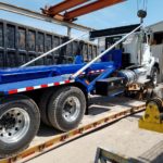 a endview photo showing a made in Canada new JT Fabrication roll off truck body being loaded on a flatbed